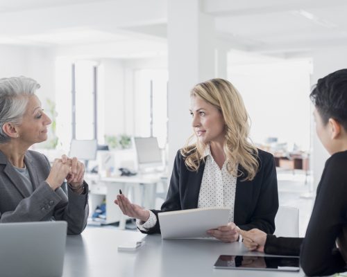 Three women in modern office with paperwork having discussion